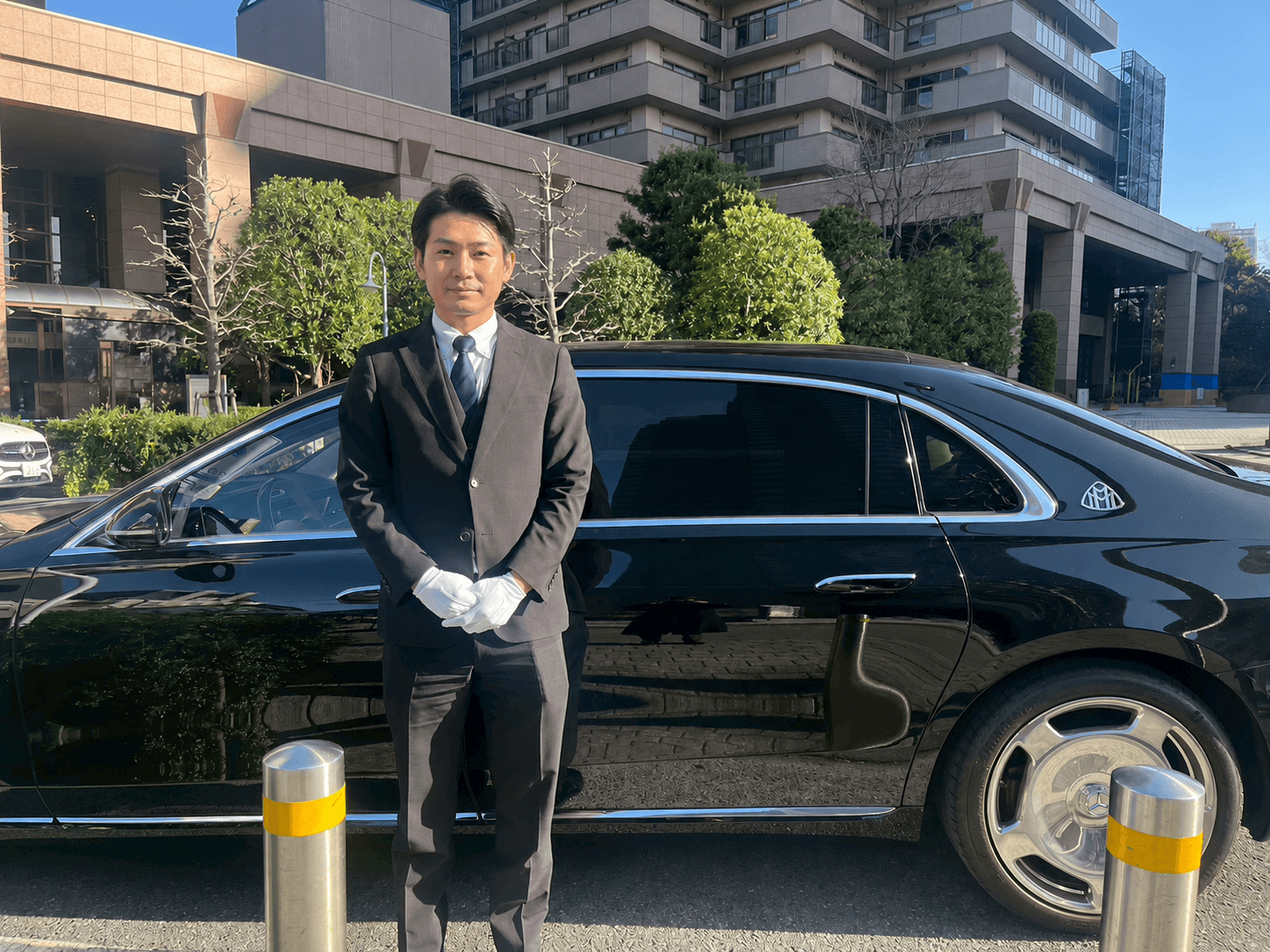 高級送迎車の前で一礼する専属ドライバー